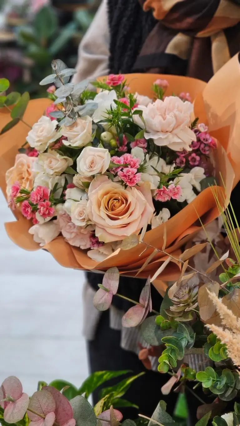 Bouquet di rose crema e pesca con garofanini rosa, incartato nella carta color terracotta