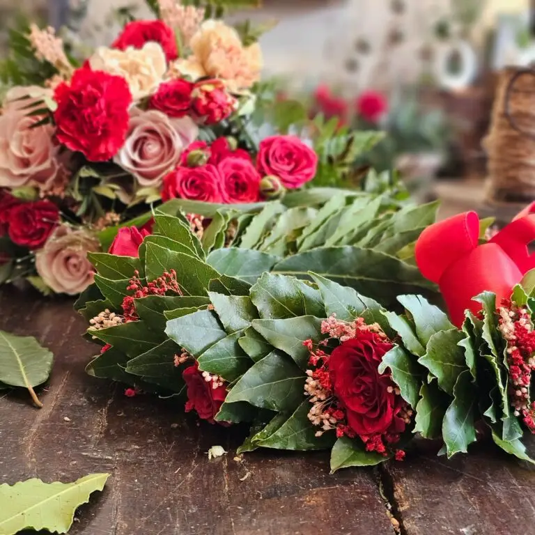 Corona di laurea in foglie di alloro con rose rosse e rosa e fiocco di raso rosso, su un tavolo di legno