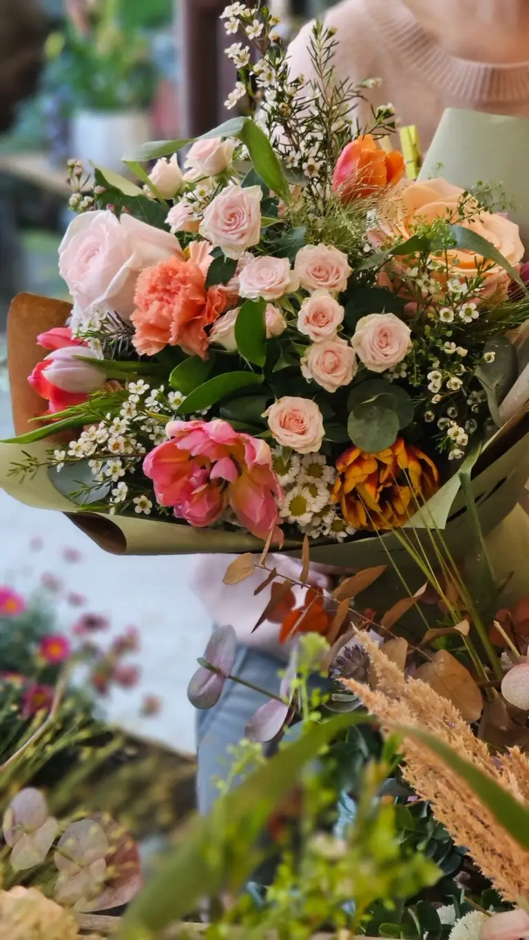 Bouquet di rose pesca, garofanini fucsia, tulipani e gypsophila, tenuto in mano davanti alla bottega