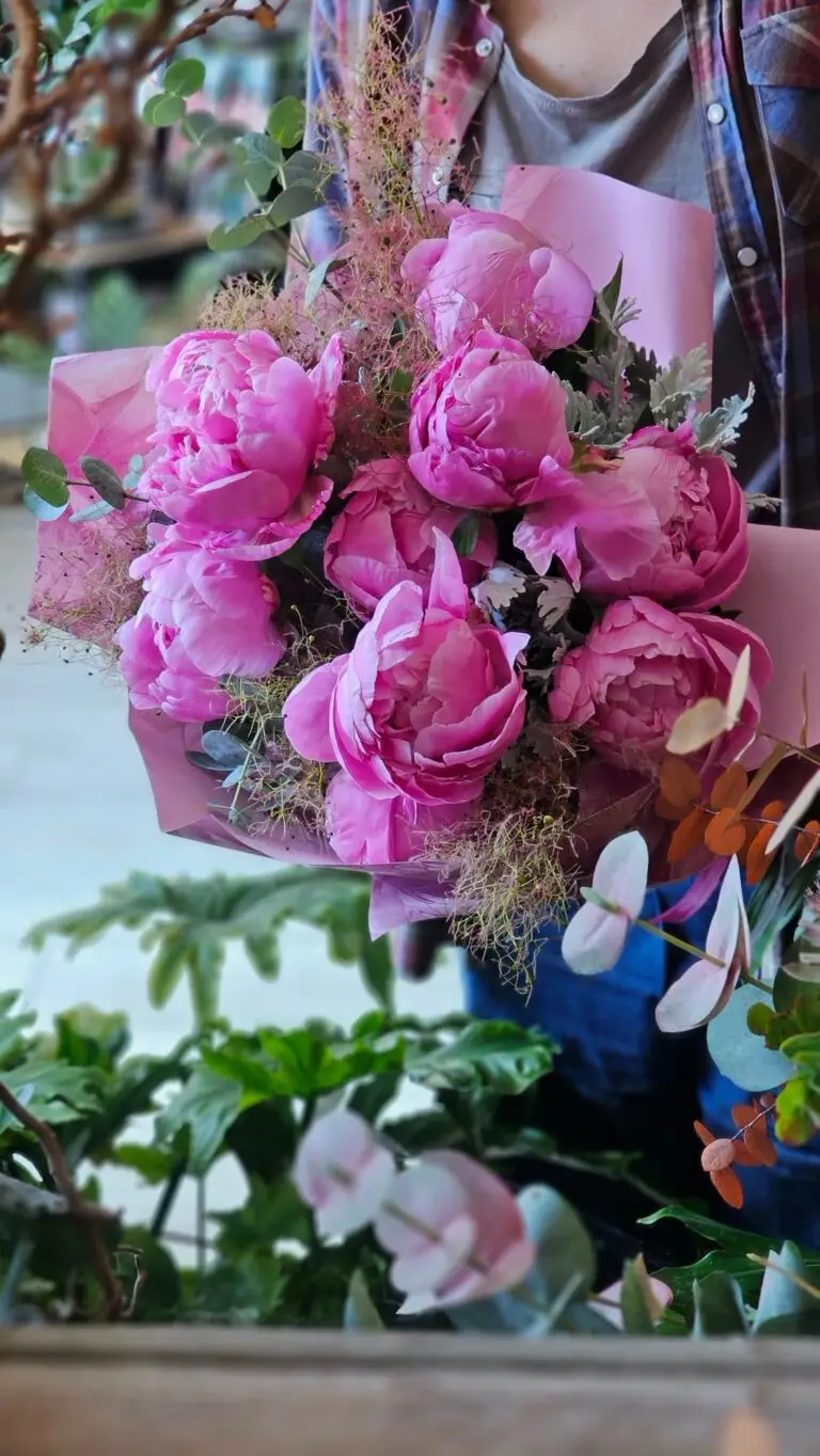 Bouquet di peonie fucsia confezionato nella carta rosa, tenuto in mano davanti alle orchidee della bottega
