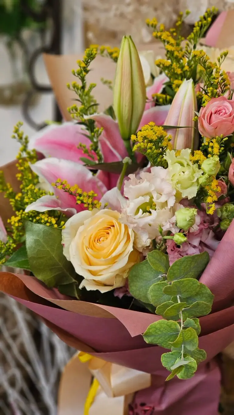 Bouquet con gigli rosa, rose color pesca e fiori gialli, confezionato nella carta bordeaux