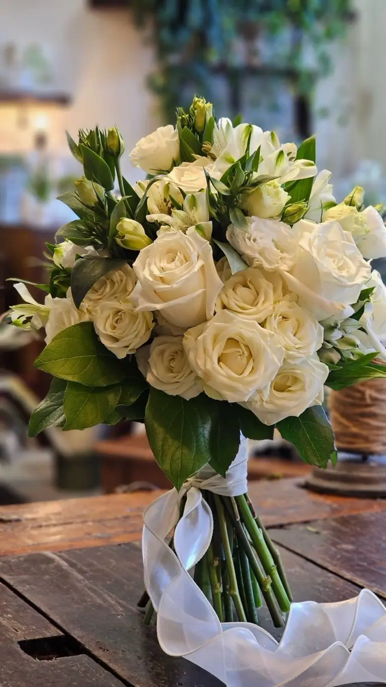 Bouquet di rose bianche e lisianthus legato con un lungo nastro di raso, su un tavolo di legno