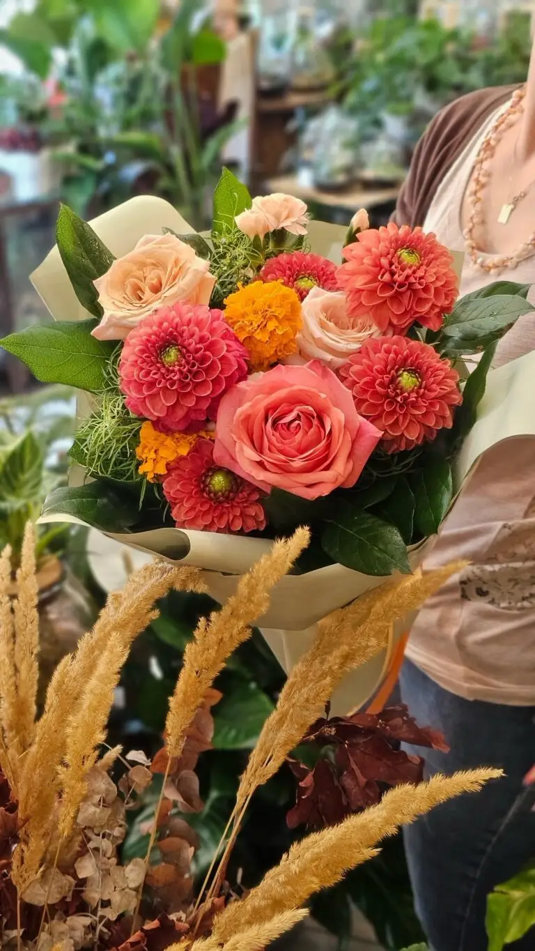 Bouquet di rose corallo e dalie arancio con spighe dorate, confezionato nella carta crema