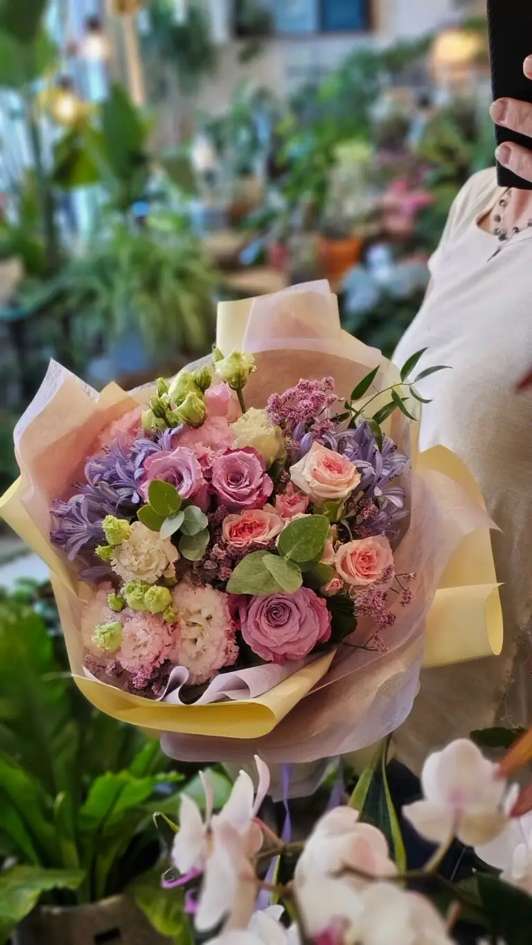 Bouquet di rose malva e rosa con lisianthus, confezionato nella carta pesca, tenuto in mano