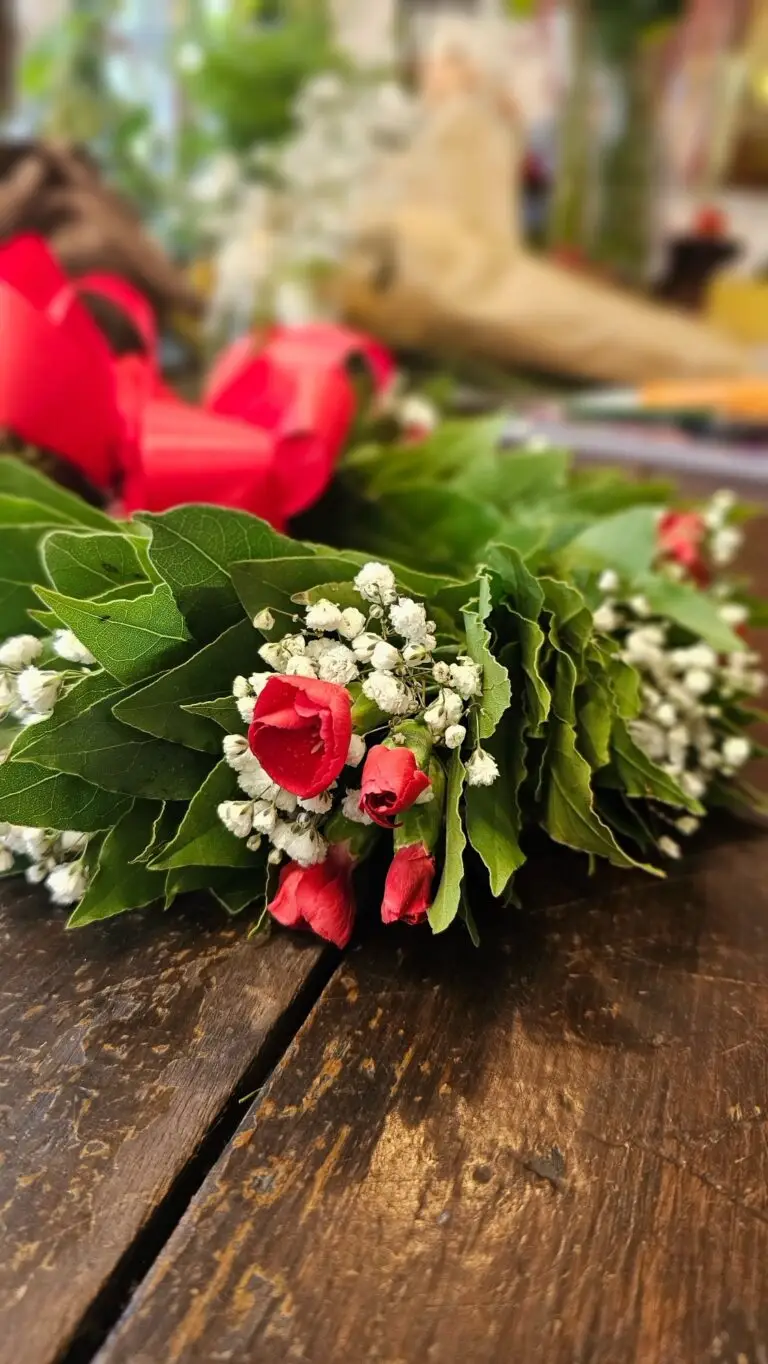 Corona di laurea in alloro vista da vicino, con anthurium rossi e fiorellini bianchi intrecciati fra le foglie