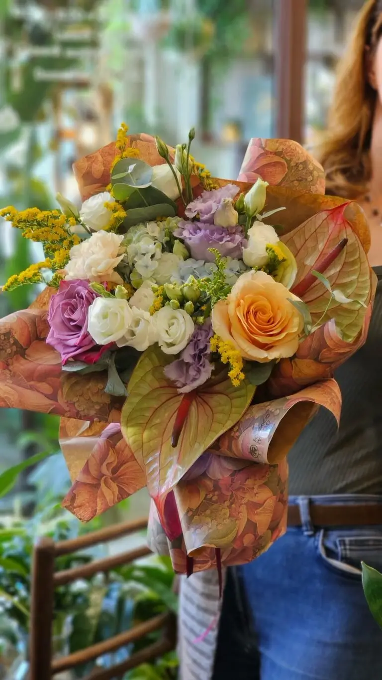 Bouquet con anthurium color pesca, rose crema, lisianthus lilla e fiori gialli, tenuto in mano