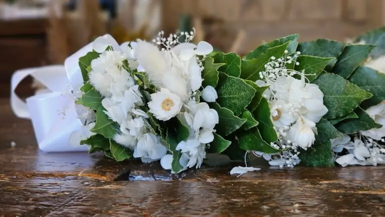 Corona di laurea in alloro con fiori bianchi e gypsophila, distesa per intero su un tavolo di legno