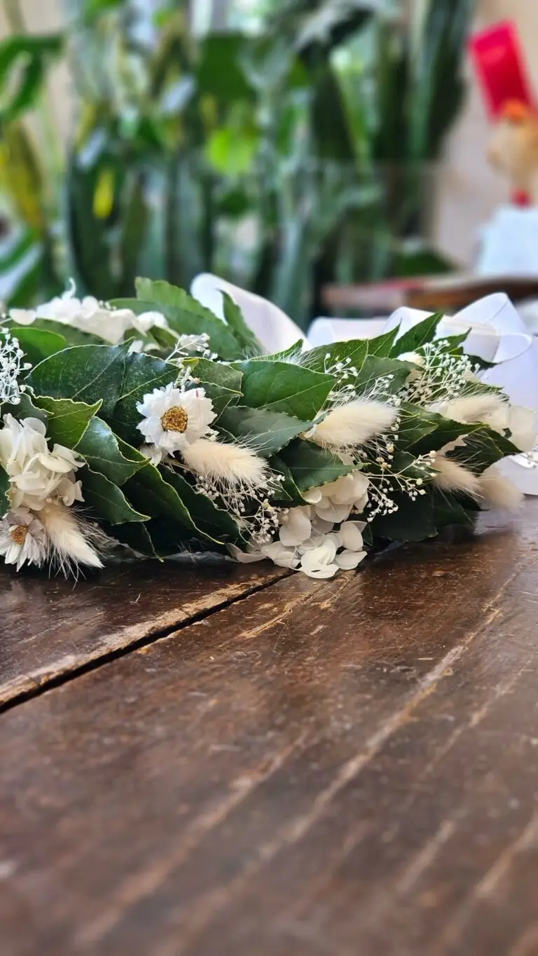 Corona di laurea in alloro con fiorellini bianchi, appoggiata su un tavolo della bottega