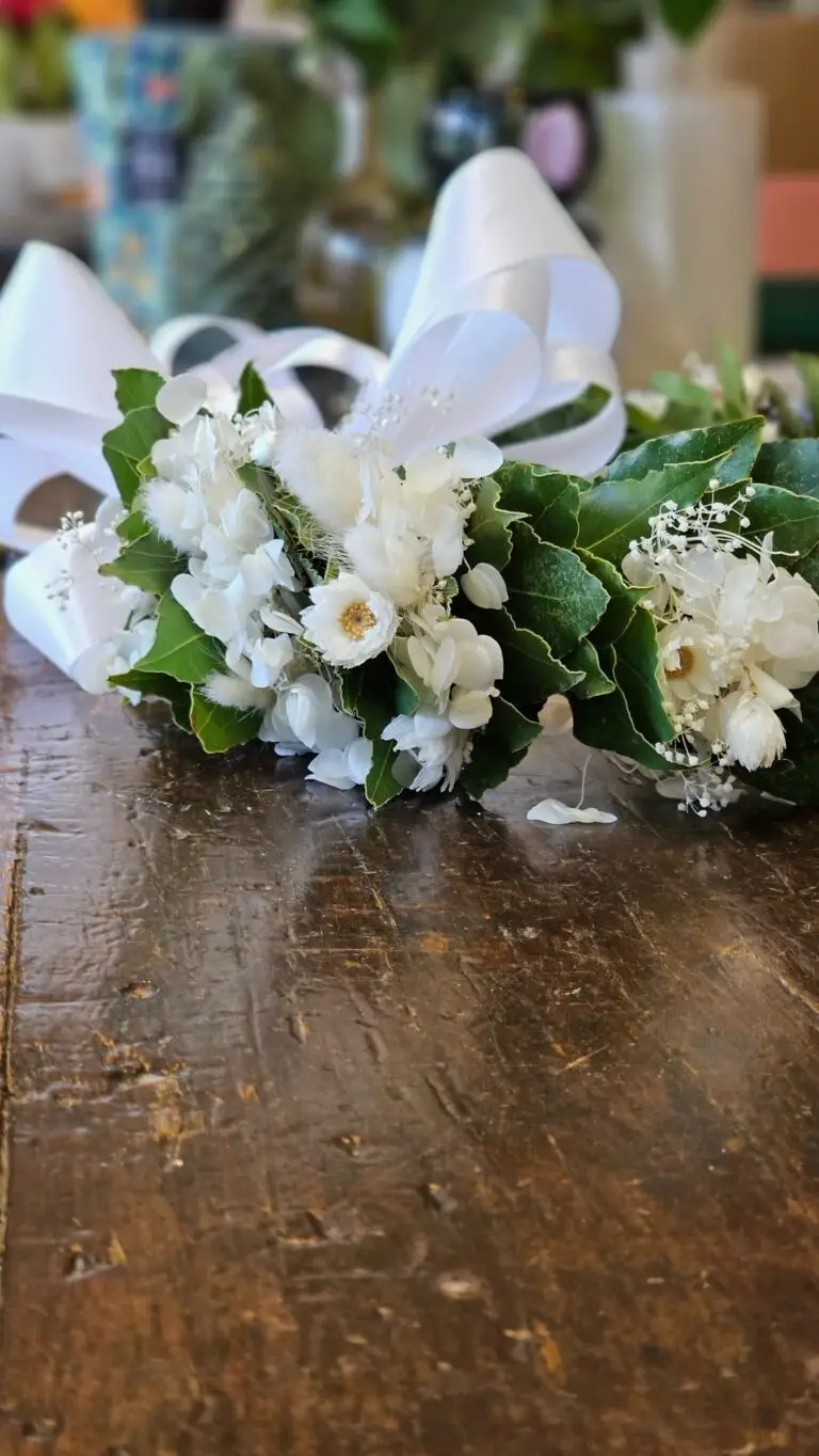 Corona di laurea in alloro con fiori bianchi e fiocco di raso, vista di lato su un tavolo di legno