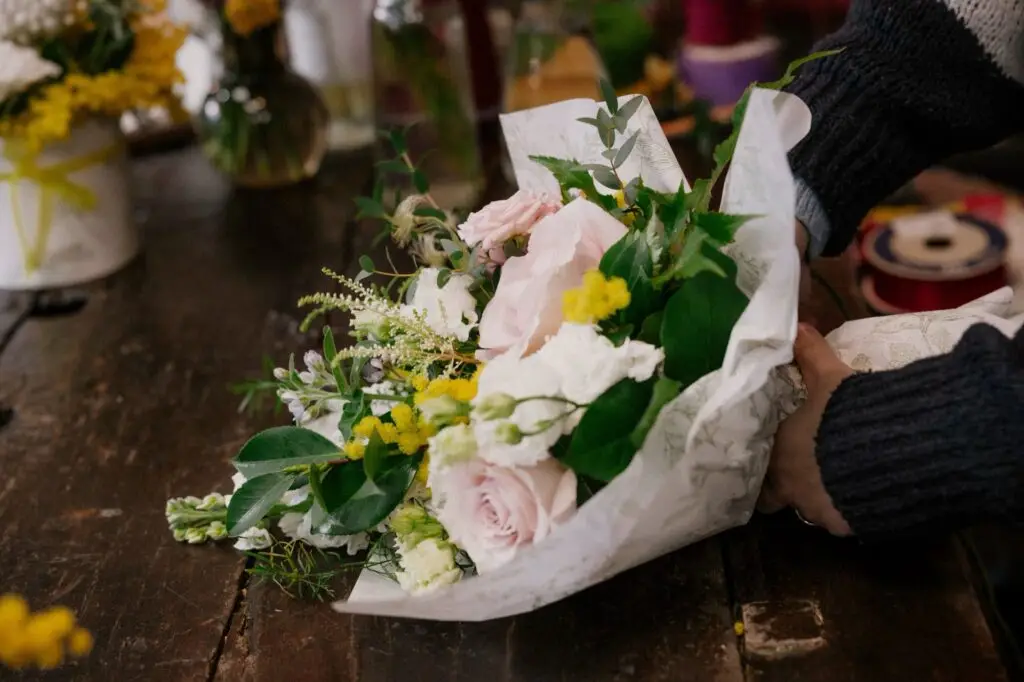 Mani che confezionano un bouquet di fiori freschi sul banco di legno della bottega
