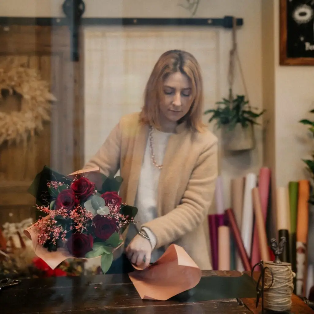 Giulia Caselli al banco della bottega mentre confeziona un bouquet, con i rotoli di carta alle spalle