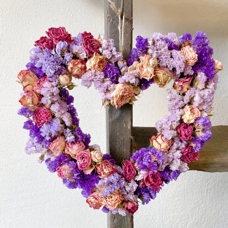Ghirlanda a cuore di fiori secchi nei toni del rosa e del lilla, appesa al muro