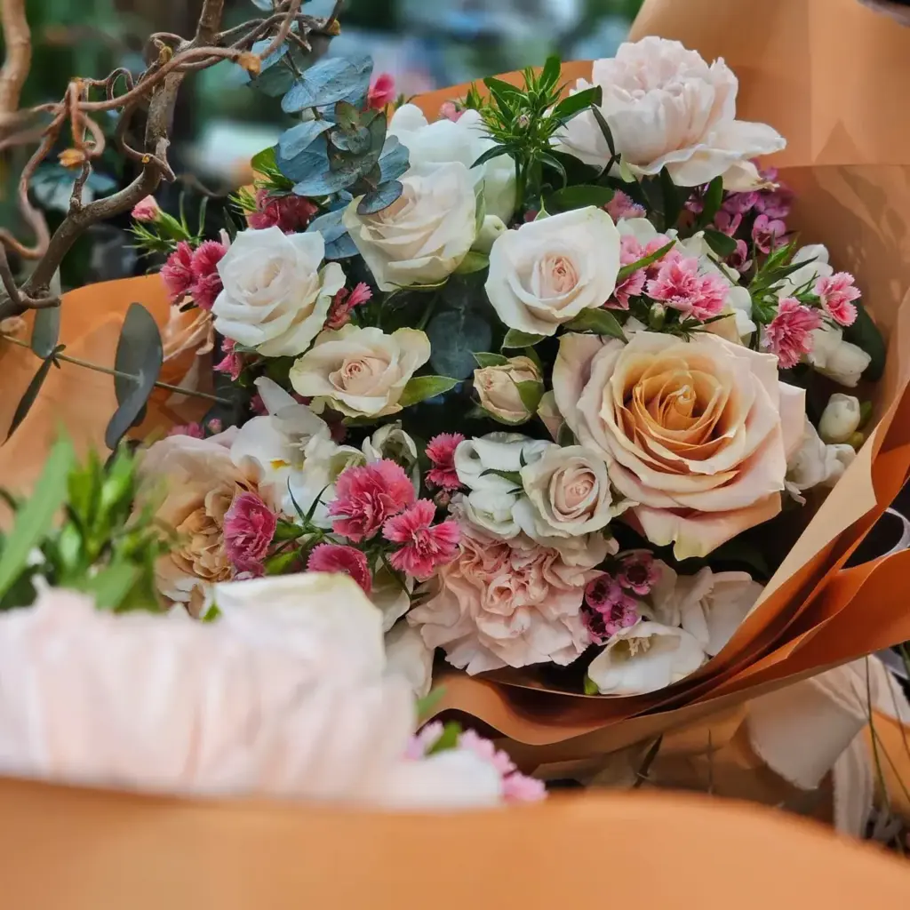 Bouquet di rose crema e garofanini rosa incartato, pronto per la consegna