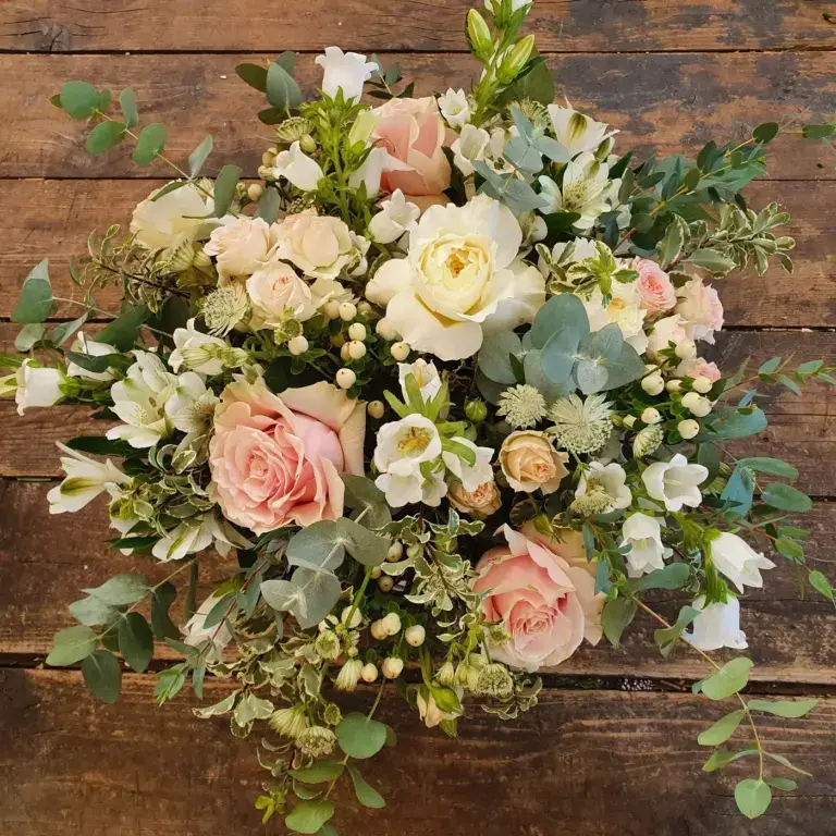 Bouquet di rose e ranuncoli nei toni del rosa e del bianco, su un banco di legno